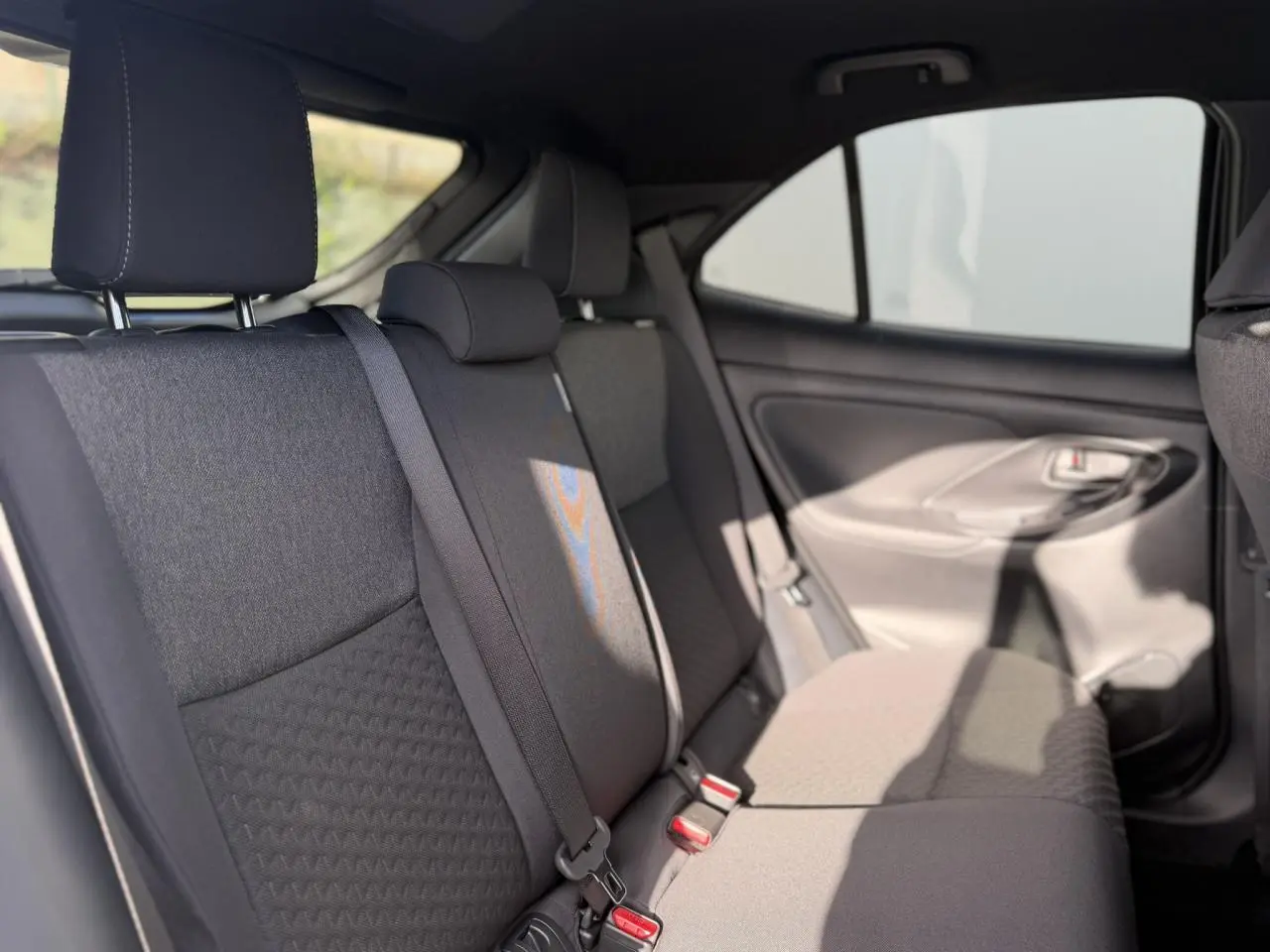 Vue intérieure de la banquette arrière côté droit de la Toyota Yaris Cross 2026 avec sièges tissu gris et ceintures de sécurité.