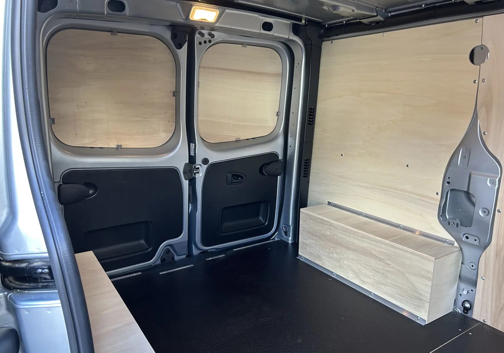 Intérieur arrière du Renault Trafic L1H1 Advance gris Highland, avec aménagement bois et plancher noir antidérapant.