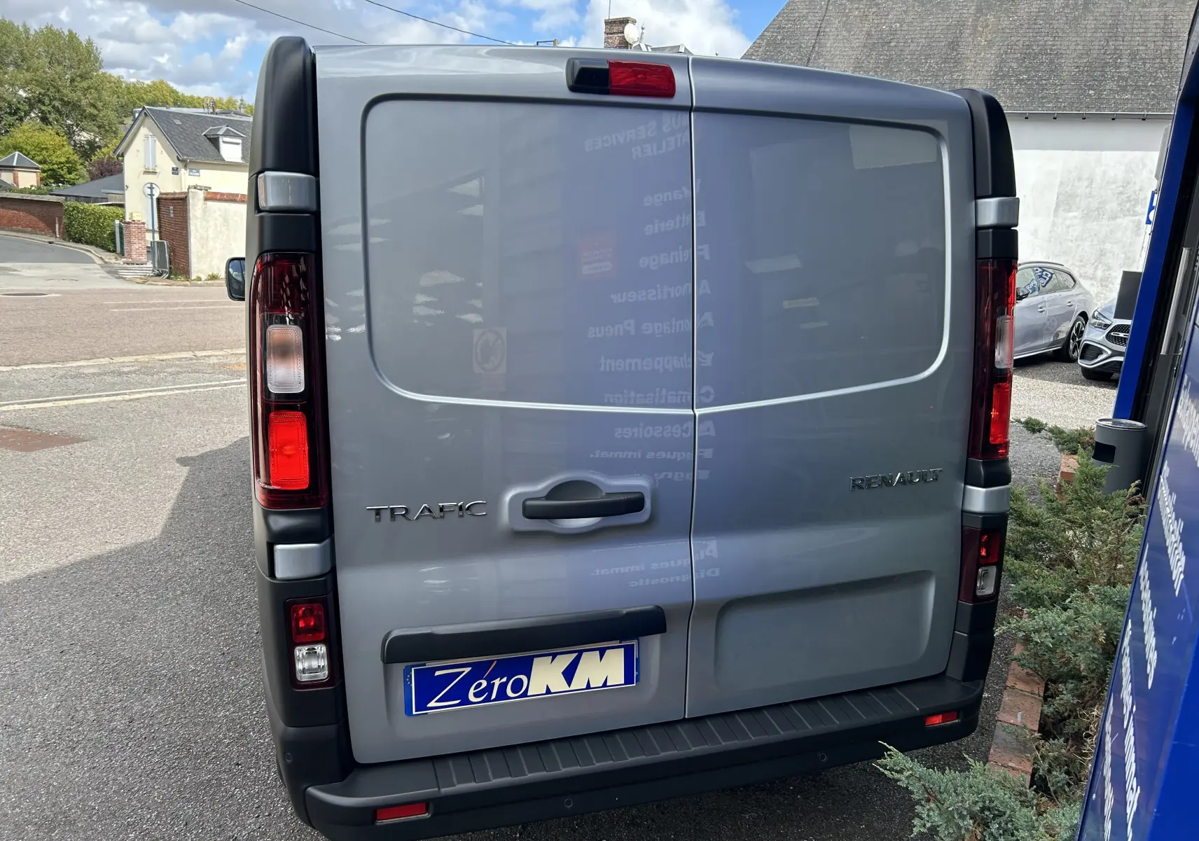 Vue arrière d'un Renault Trafic Fourgon gris Highland avec feux arrière verticaux et plaque Zero KM visible.
