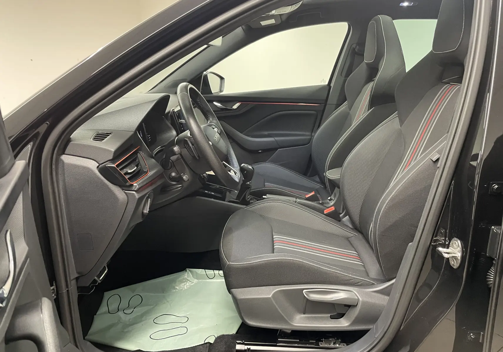 Vue intérieure côté conducteur de la Skoda Scala 1.5 TSI 150 DSG7 Monte-Carlo noire avec sièges sport et surpiqûres rouges.