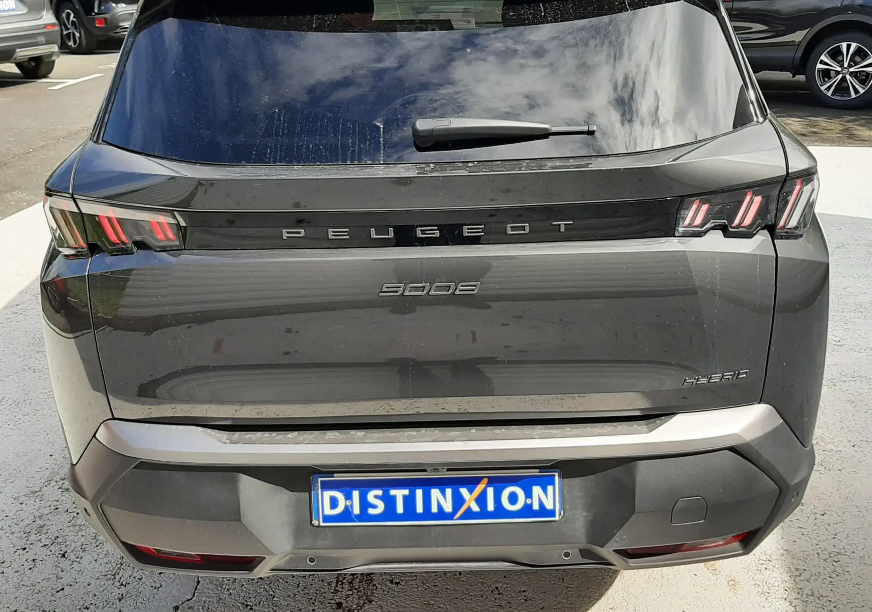 Vue arrière d’un Peugeot 5008 gris titane métal 2025 avec feux LED caractéristiques et logo central visible.
