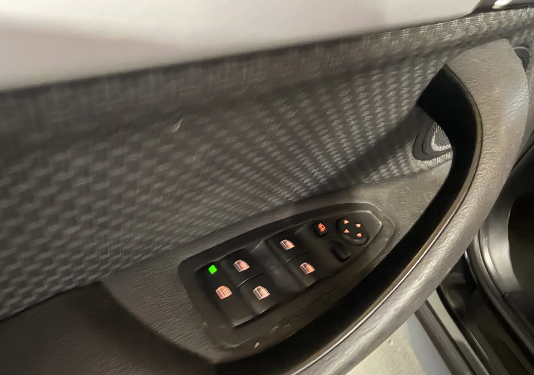 Détail des commandes des vitres électriques côté conducteur dans une BMW X1 noire, version 2019, vue intérieure rapprochée.