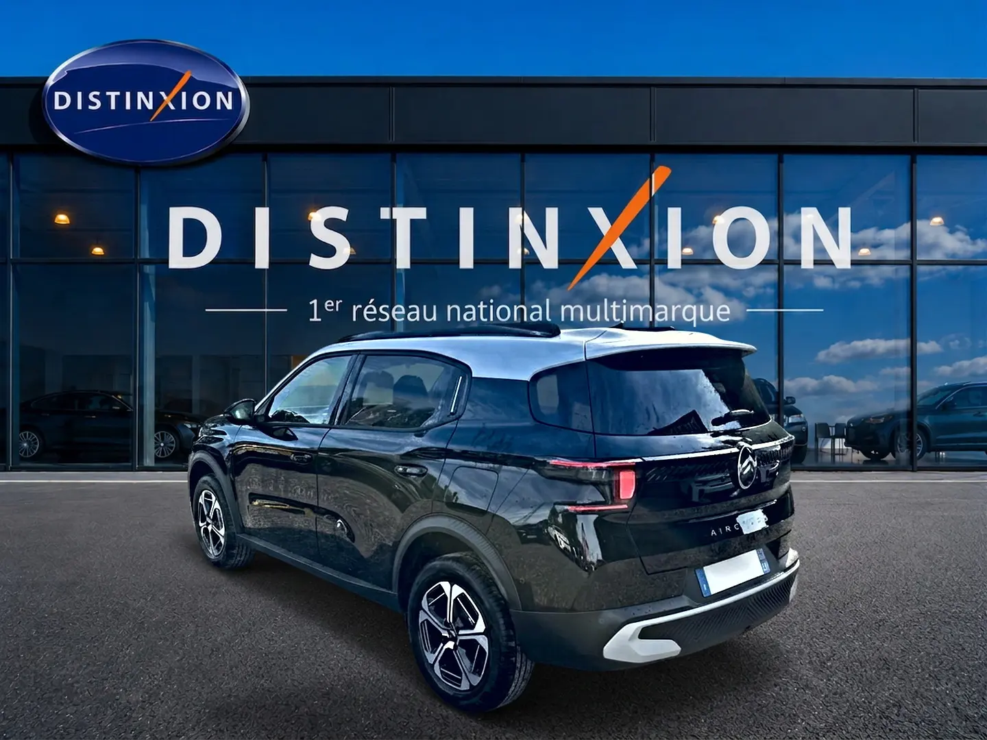 Vue 3/4 arrière droite d'une Citroën C3 Aircross noire 2026 avec toit clair et jantes alu, devant une vitrine Distinxion.