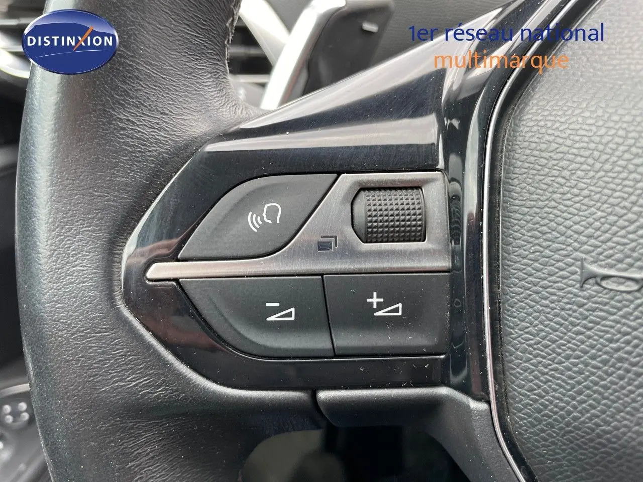 Gros plan sur les commandes du volant en cuir noir du Peugeot 3008 gris, avec boutons de volume et appel mains libres.