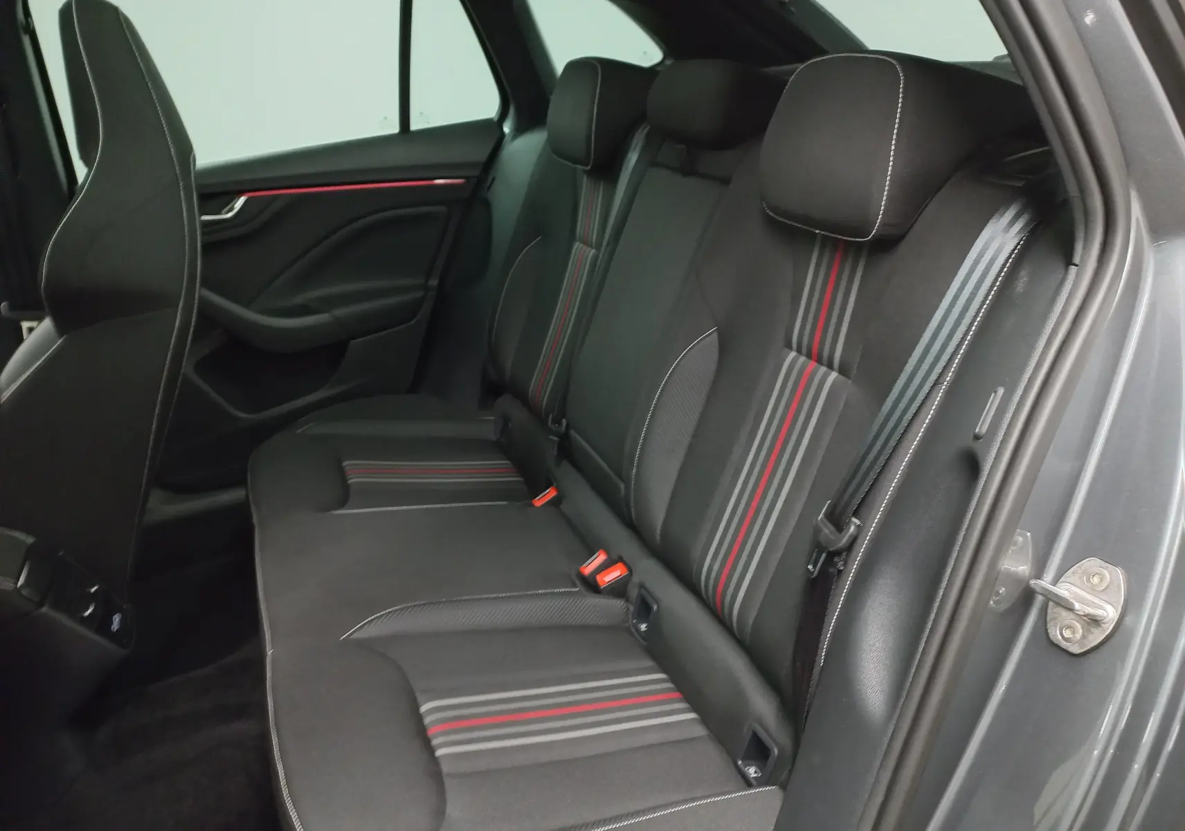 Vue intérieure arrière droite des sièges arrière noirs avec surpiqûres blanches et bandes rouges d'une Skoda Scala 2025 Gris Graphite.