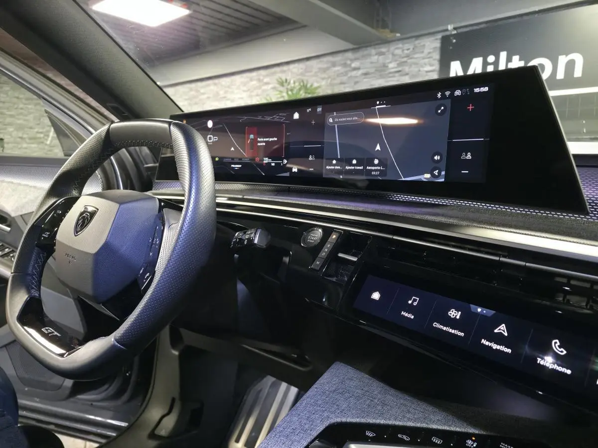 Vue intérieure côté conducteur du tableau de bord noir et écran panoramique du Peugeot 5008 gris hybride 2025.