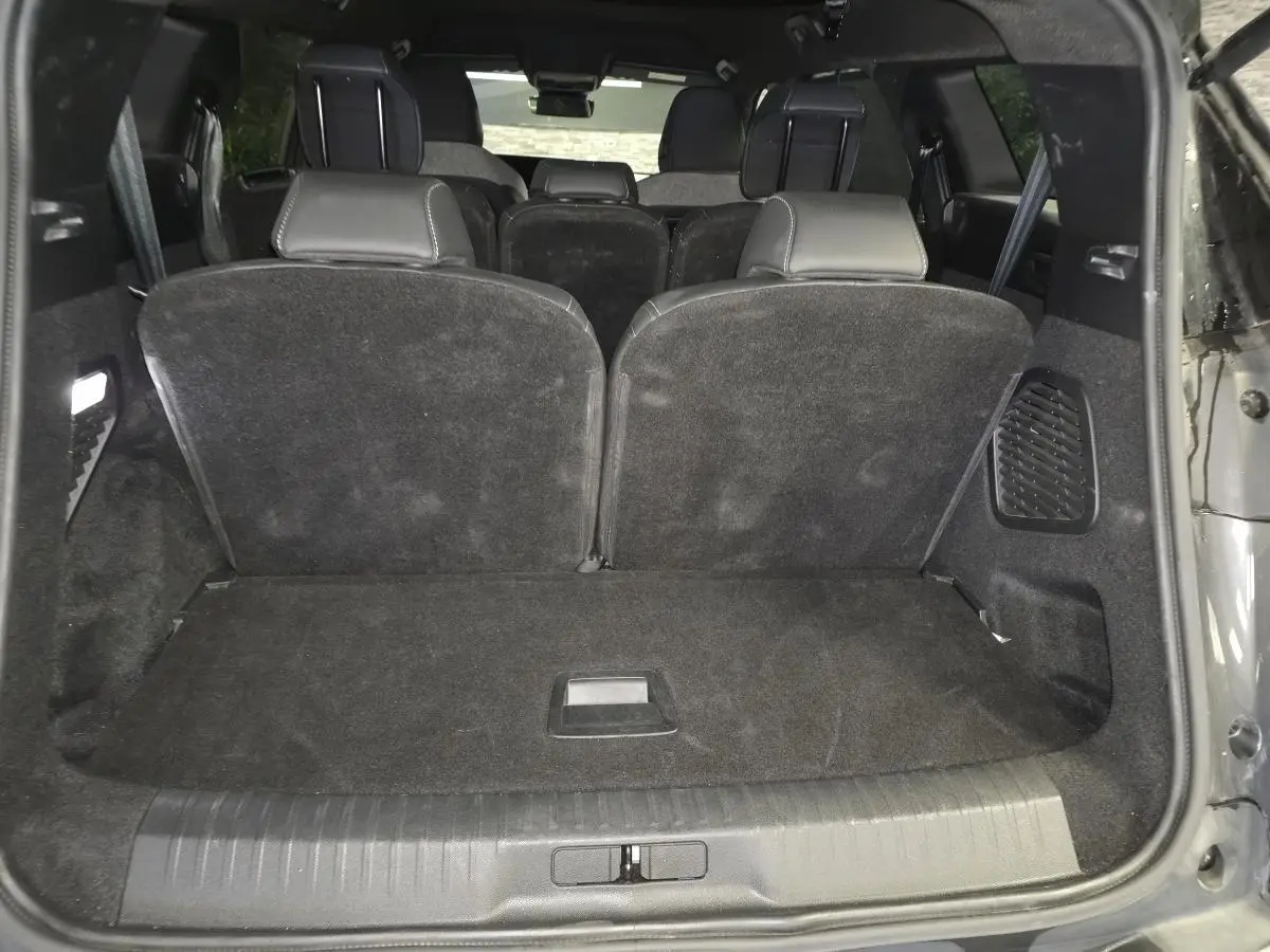 Coffre ouvert vu de l'arrière d'un Peugeot 5008 gris, montrant la banquette arrière en tissu noir relevée.