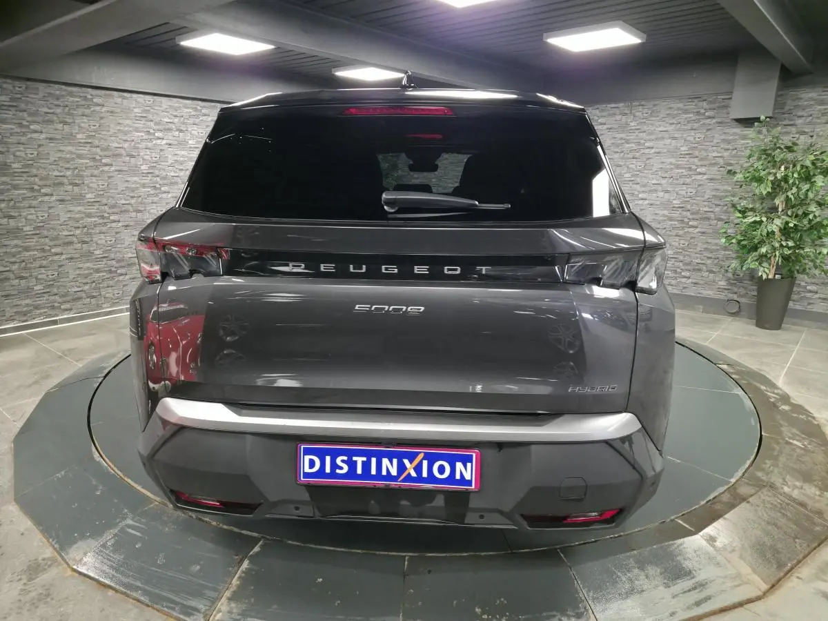 Vue arrière d'un Peugeot 5008 gris métallisé avec bandeau noir laqué et feux arrière 3 griffes LED en intérieur showroom.