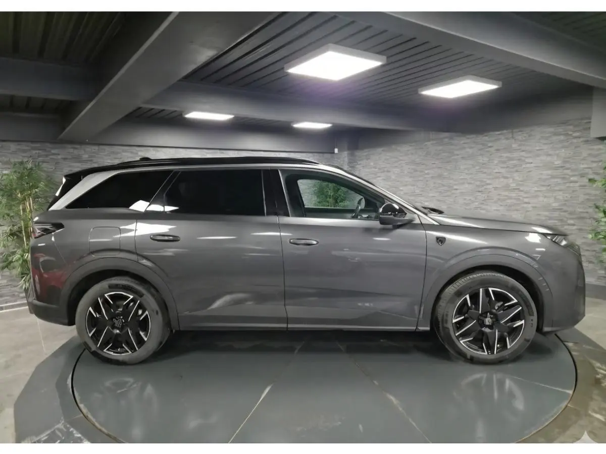 Vue de profil côté gauche d'un Peugeot 5008 gris métallisé 2025 en hybride essence, avec jantes alliage noires et toit noir.