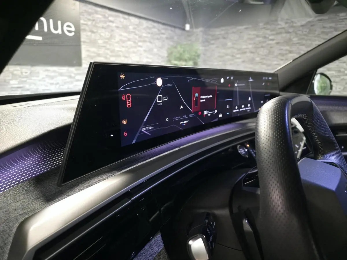 Vue intérieure du tableau de bord et écran numérique panoramique du Peugeot 5008 gris hybride, avec volant perforé noir.