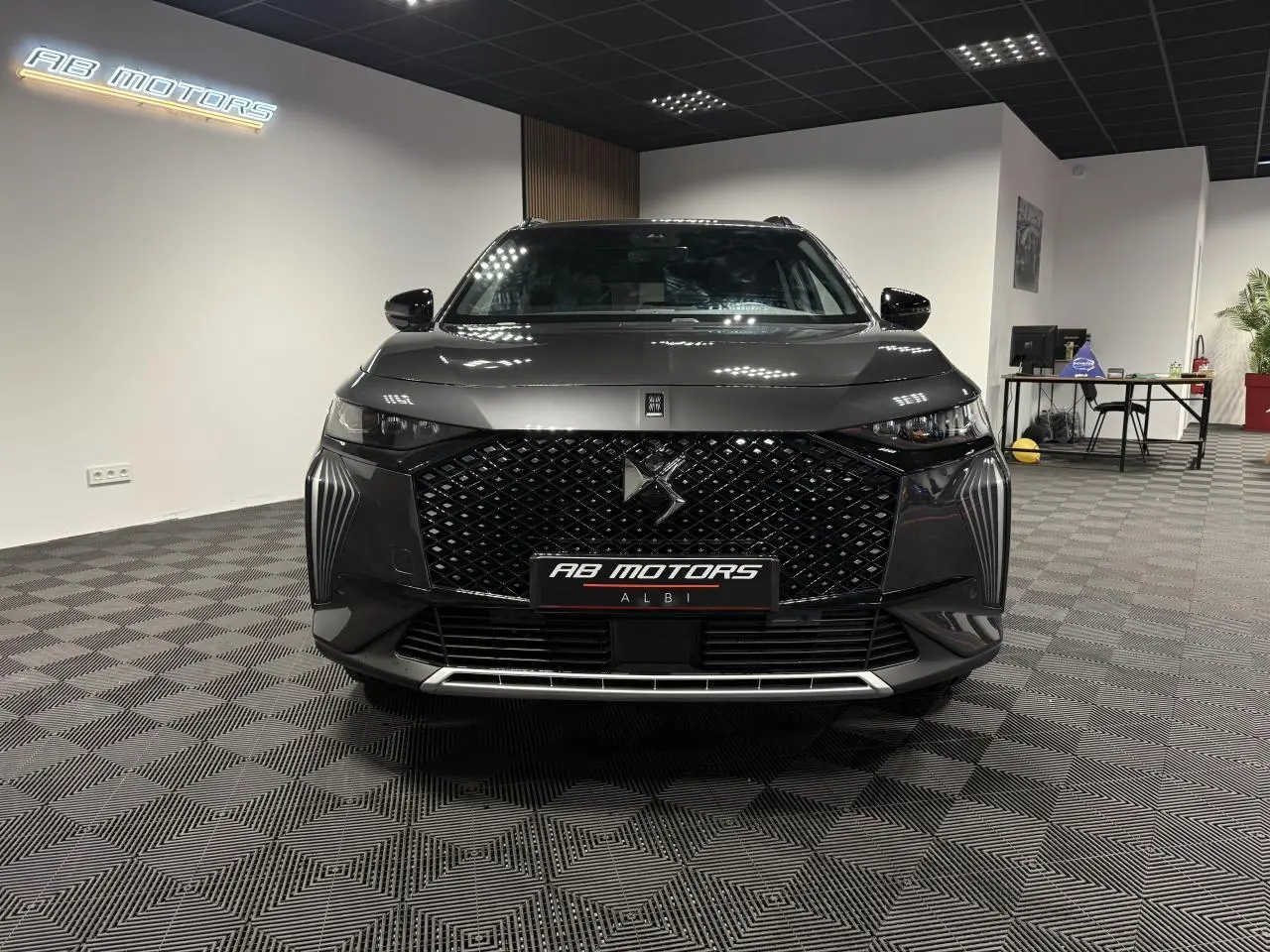 Vue avant d'un DS7 Crossback gris métallisé avec calandre noire à motifs losanges et logo DS central, en showroom.