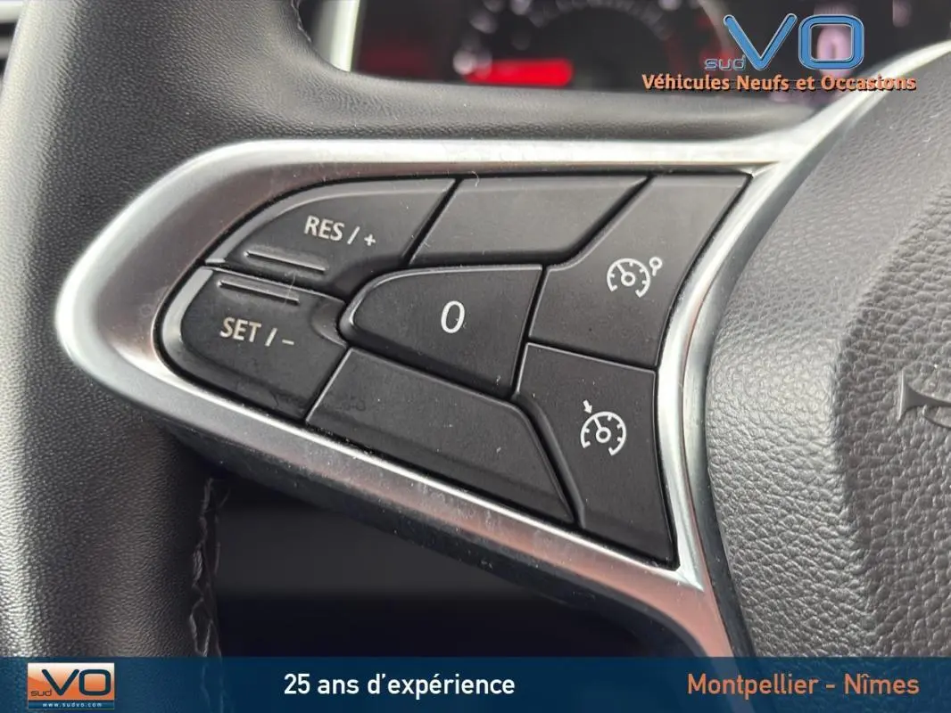 Gros plan sur les commandes du régulateur de vitesse au volant d'une Renault Clio V Blue dCi 85 Business gris foncé.