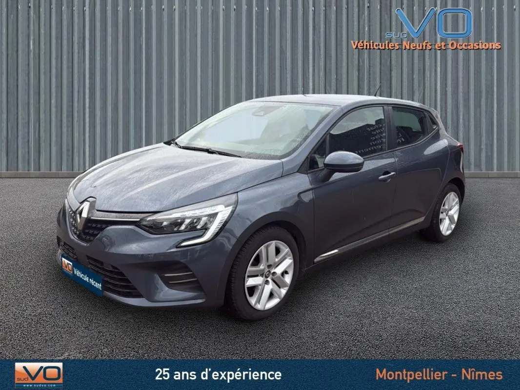 Renault Clio V Blue dCi 85 Business gris foncé vue 3/4 avant droit sur sol bitumé devant un mur métallique.