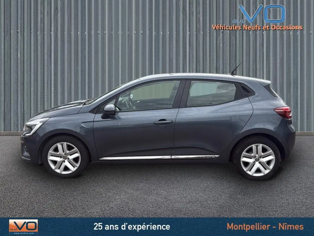 Profil côté gauche d'une Renault Clio V Blue dCi 85 Business gris foncé, vue extérieure sur fond industriel.