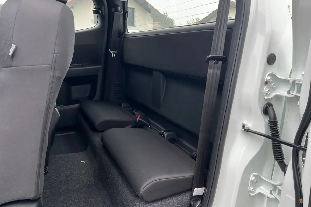 Vue intérieure arrière du pick-up Isuzu D-MAX Splash white, montrant les strapontins rabattables et la porte ouverte côté droit.
