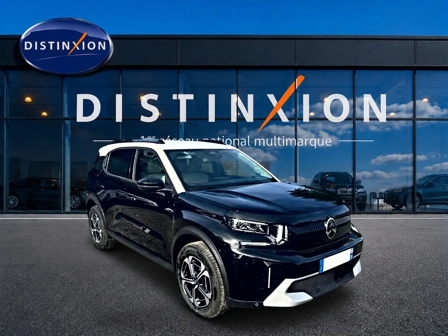 Vue 3/4 avant droite d'un Citroën C3 Aircross noir avec toit blanc et jantes alu devant un showroom Distinxion.