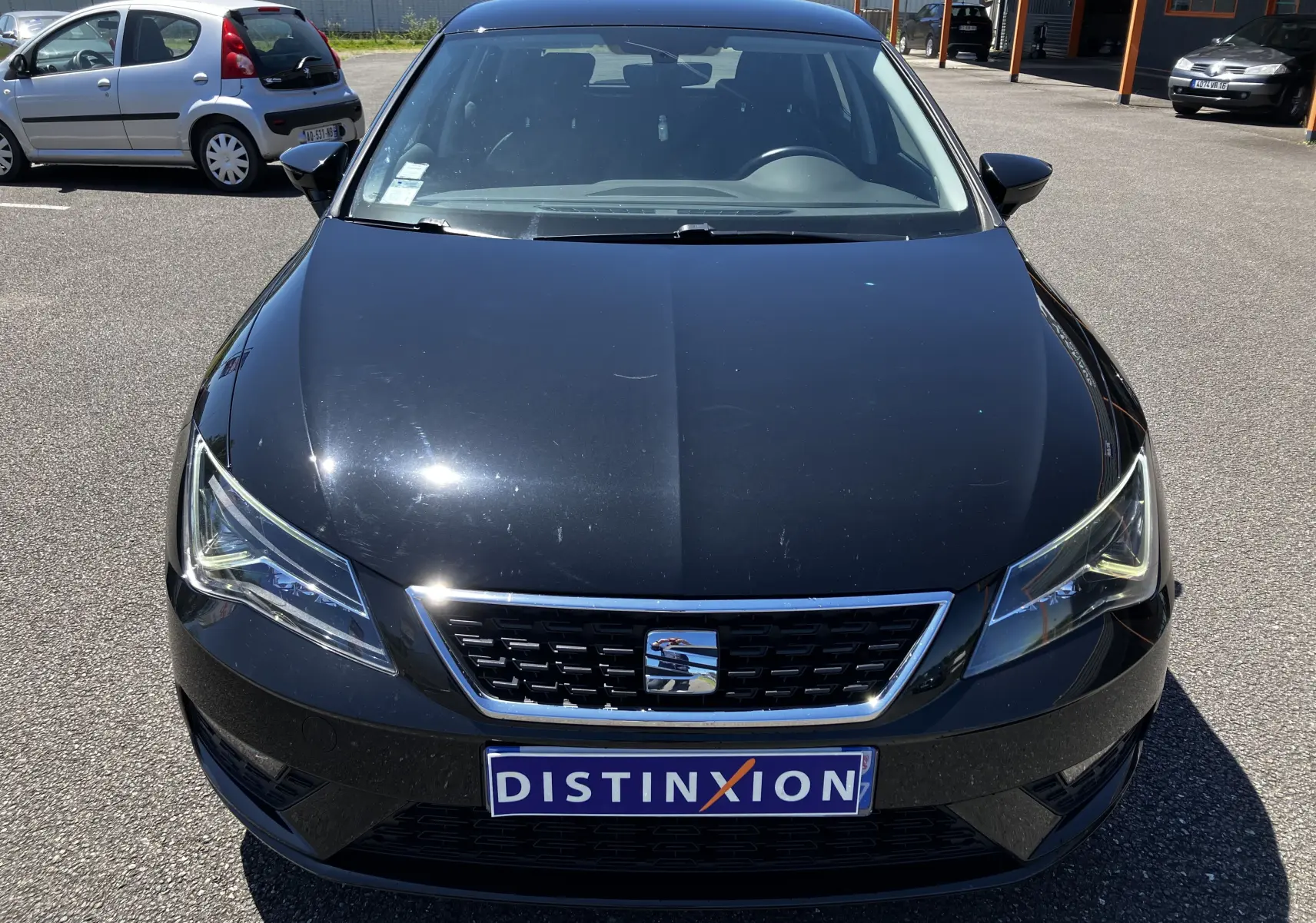 Vue frontale d'une SEAT LEON noire 2018 avec calandre chromée et plaque Distinxion visible sur un parking.