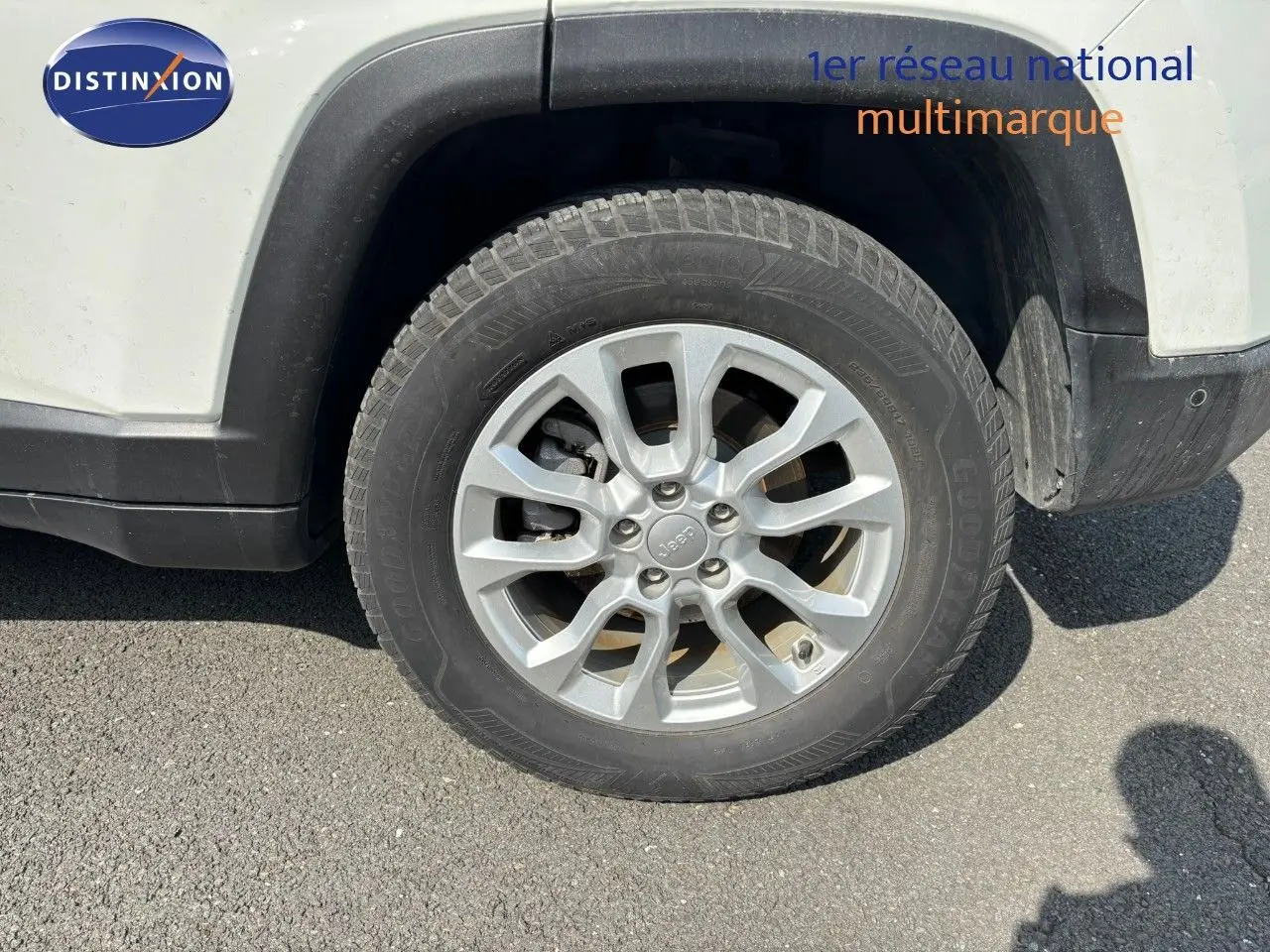 Gros plan sur la roue avant droite d'un Jeep Compass blanc, mettant en valeur la jante alliage et le pneu Goodyear.