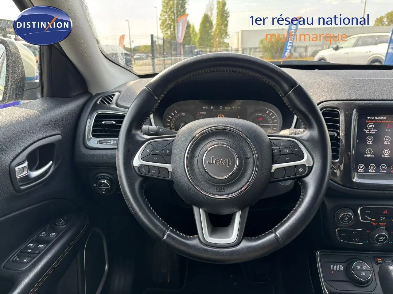 Vue intérieure centrée sur le volant cuir noir du Jeep Compass blanc, avec tableau de bord et écran tactile visibles.