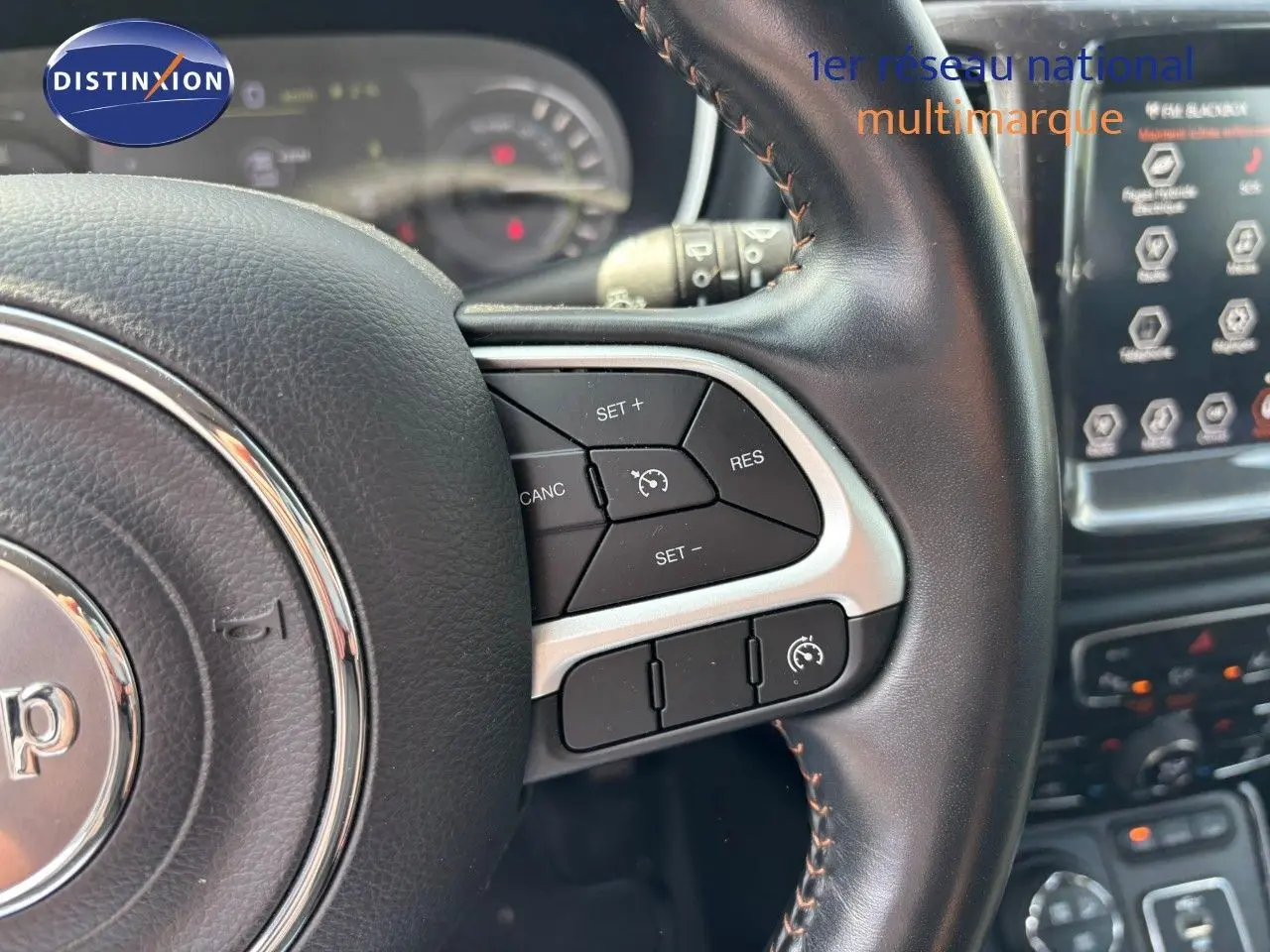 Gros plan sur le volant cuir noir du Jeep Compass blanc, mettant en valeur les commandes de régulateur de vitesse.