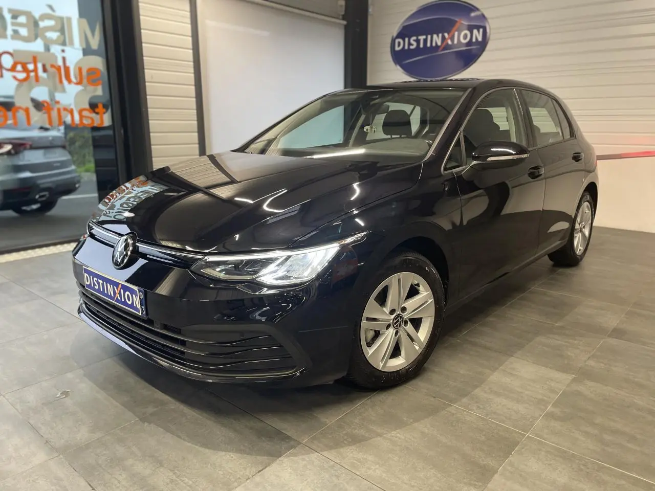 Volkswagen Golf 1.5 eTSI noire vue 3/4 avant en intérieur avec jantes alliage et logo lumineux sur calandre.