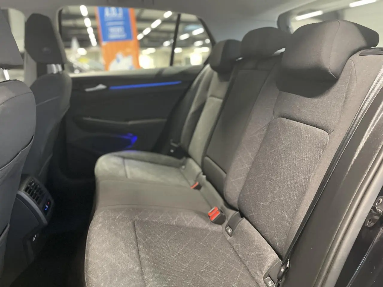 Vue intérieure côté droit des sièges arrière gris foncé de la Volkswagen Golf 1.5 eTSI Style 2024 avec éclairage d'ambiance bleu.