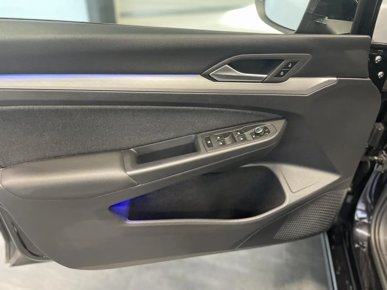 Panneau de porte avant gauche noir de Volkswagen Golf 1.5 eTSI 2024 avec éclairage d'ambiance bleu et commandes électriques.