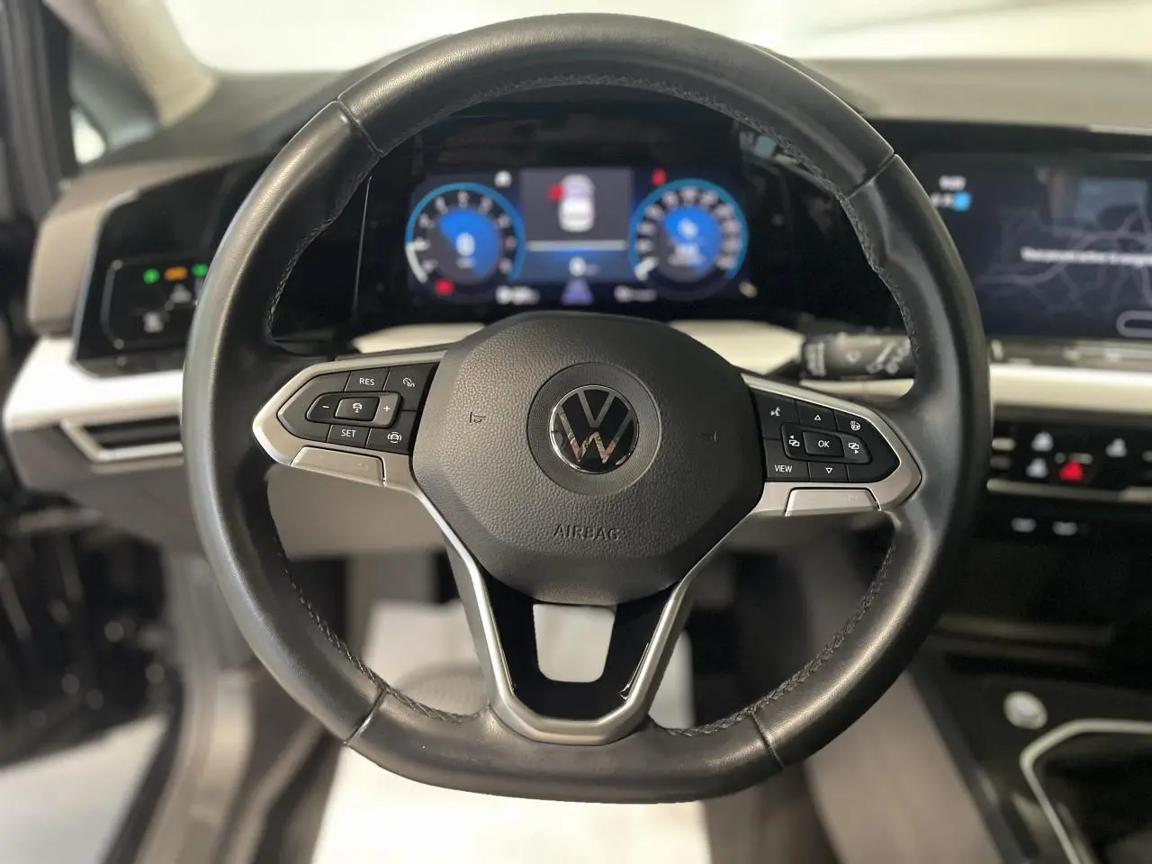 Vue rapprochée du volant noir en cuir de la Volkswagen Golf 1.5 eTSI 2024 avec tableau de bord digital lumineux.