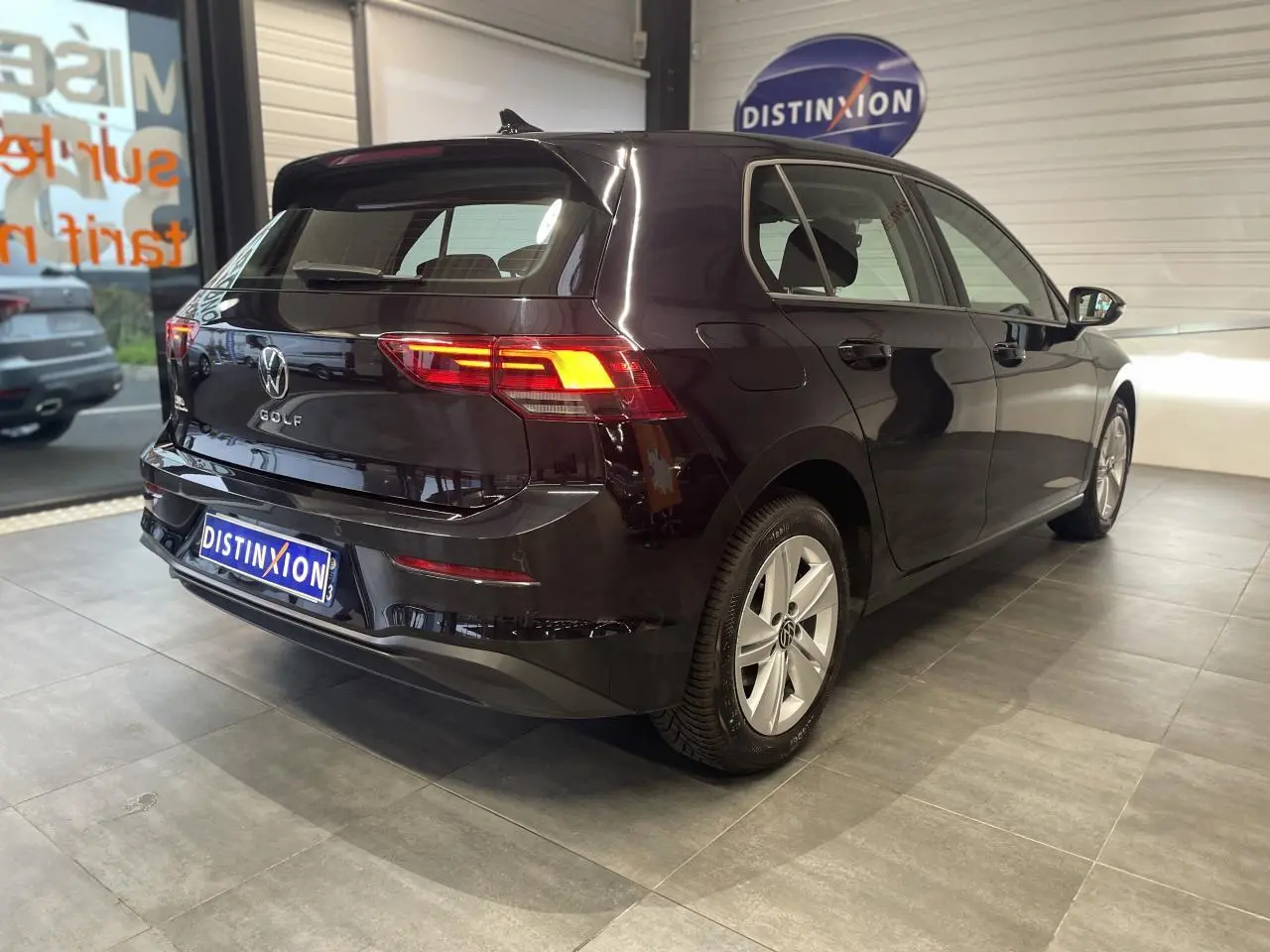 Volkswagen Golf 1.5 eTSI noire vue 3/4 arrière droit en intérieur avec feux arrière allumés et jantes alliage.