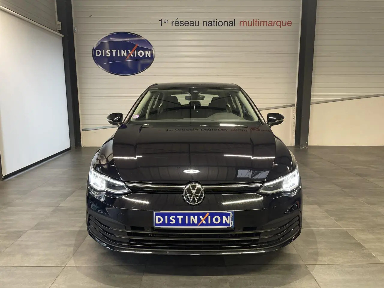 Volkswagen Golf 2024 noire vue de face avec phares LED allumés dans un showroom intérieur.