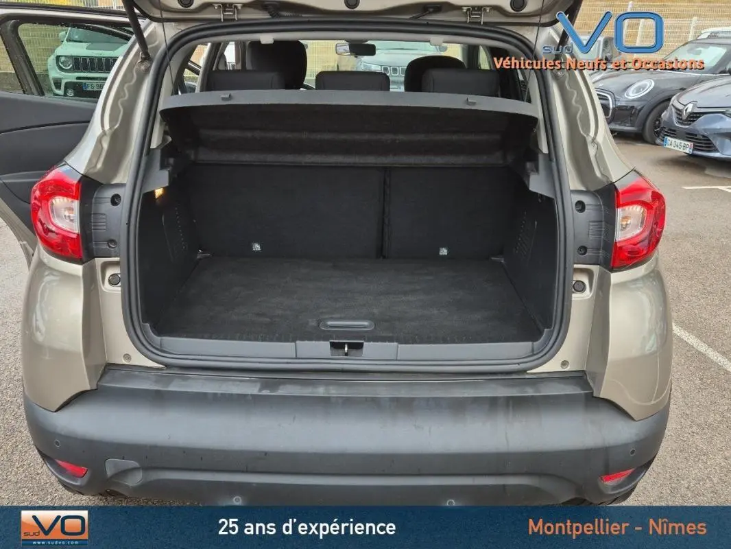 Coffre ouvert vu de l'arrière d'un Renault Captur gris 2014, montrant l'espace de chargement et la plage arrière relevée.