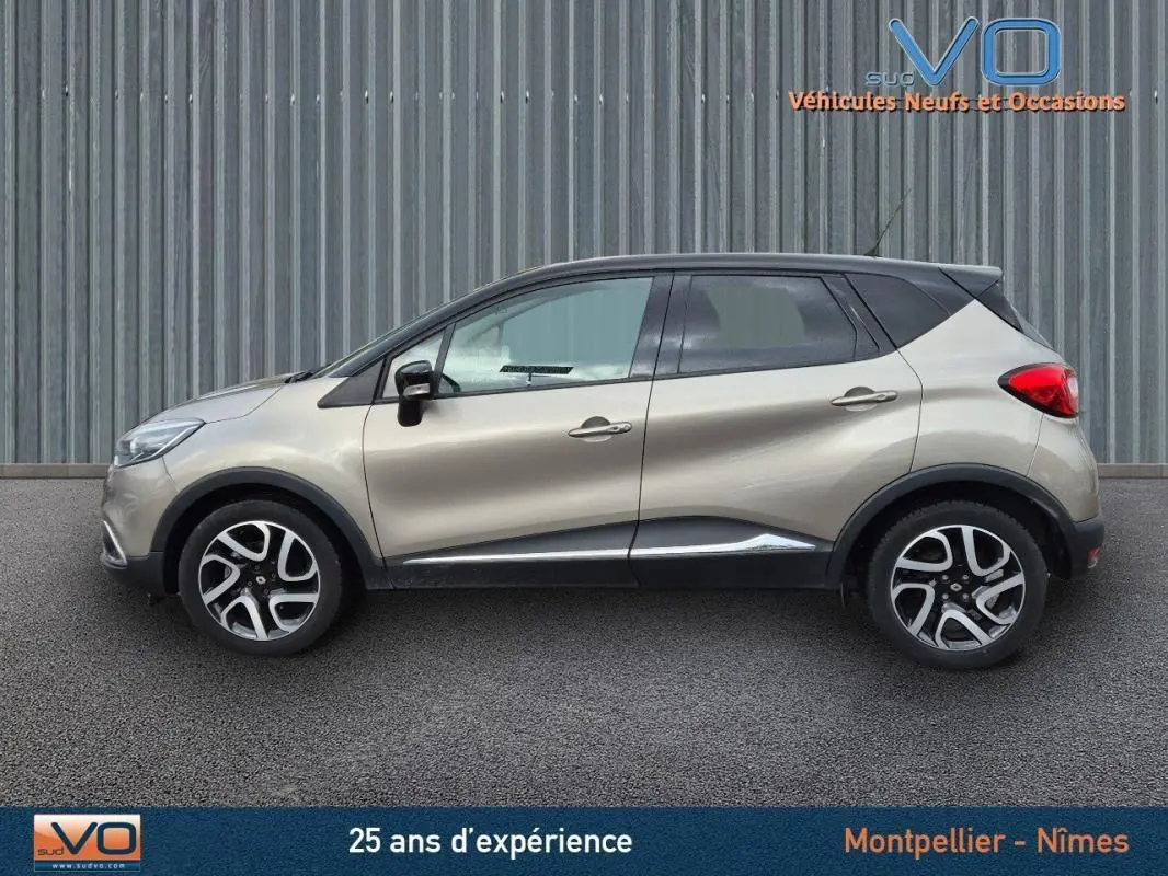 Profil côté gauche d'un Renault Captur gris 2014 avec toit noir et jantes alliage 17 pouces sur fond industriel.