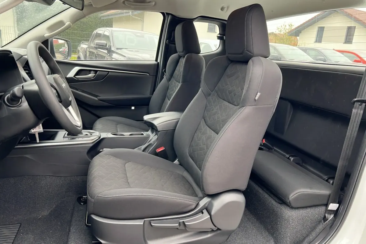 Vue intérieure côté gauche du pick-up Isuzu D-MAX 2026 Splash white, montrant les sièges avant en tissu gris foncé et l'accoudoir central.