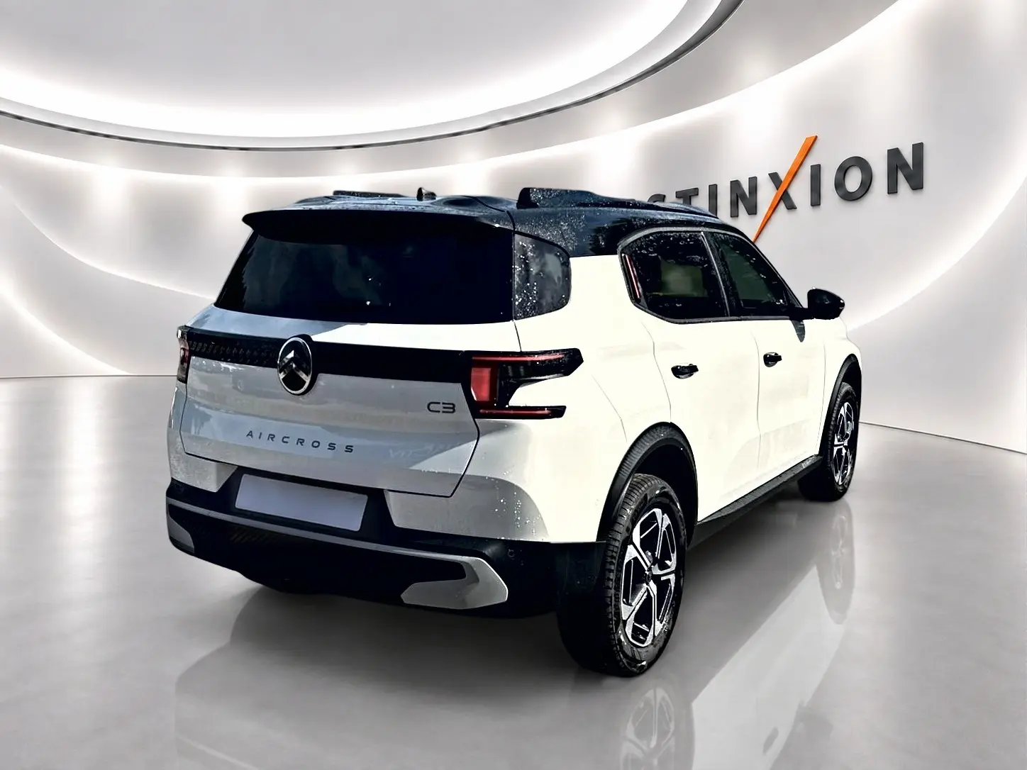 Vue 3/4 arrière droite d'un Citroën C3 Aircross blanc avec toit noir et jantes alu modernes dans un showroom.