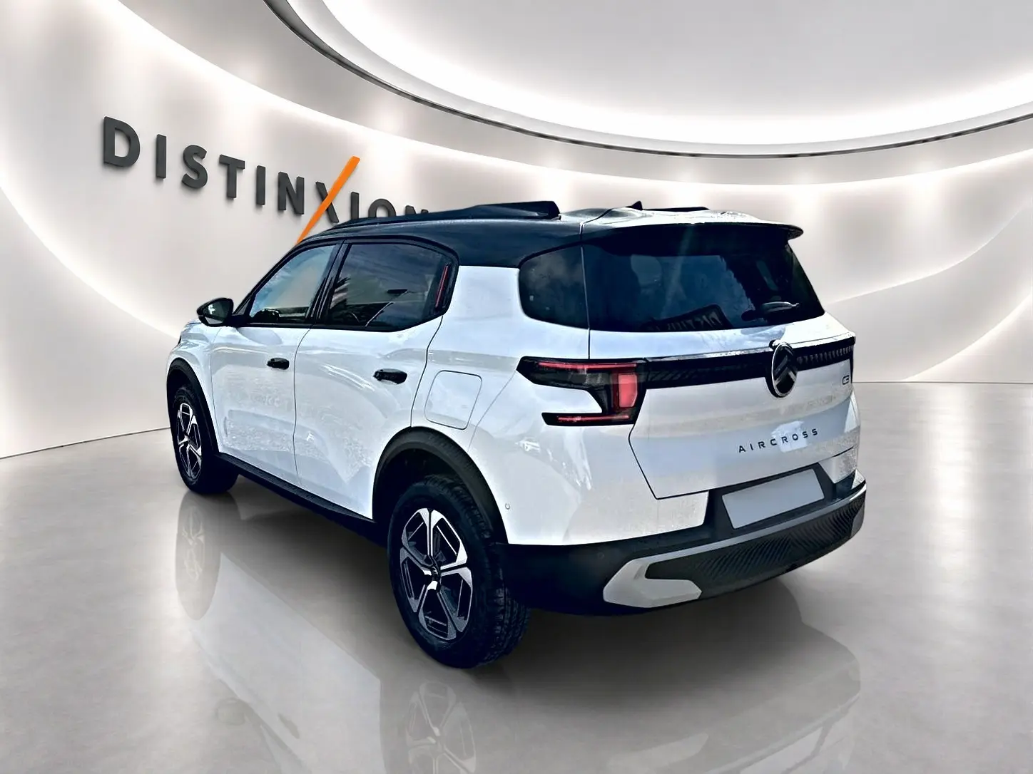 Vue 3/4 arrière droite d'un Citroën C3 Aircross blanc avec toit noir et jantes alu noires en showroom.