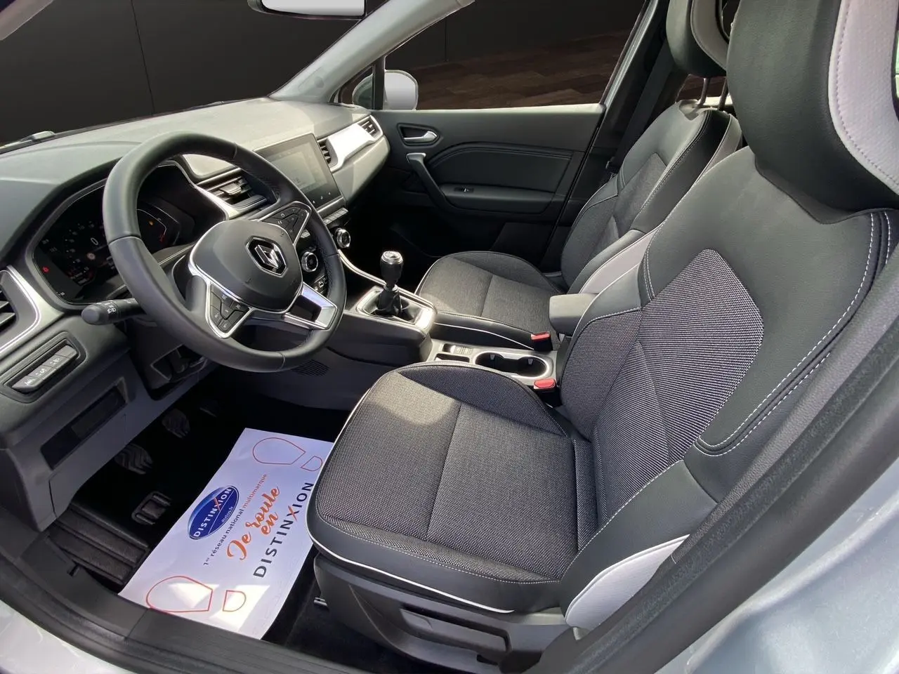Vue intérieure côté conducteur du Renault Captur TCE 90 Techno 2024, sellerie tissu gris et console centrale avec boîte manuelle.