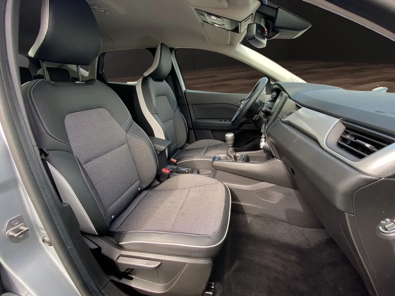 Vue intérieure côté conducteur du Renault Captur TCE 90 TECHNO 2024, sièges tissu noir avec surpiqûres grises et tableau de bord gris.