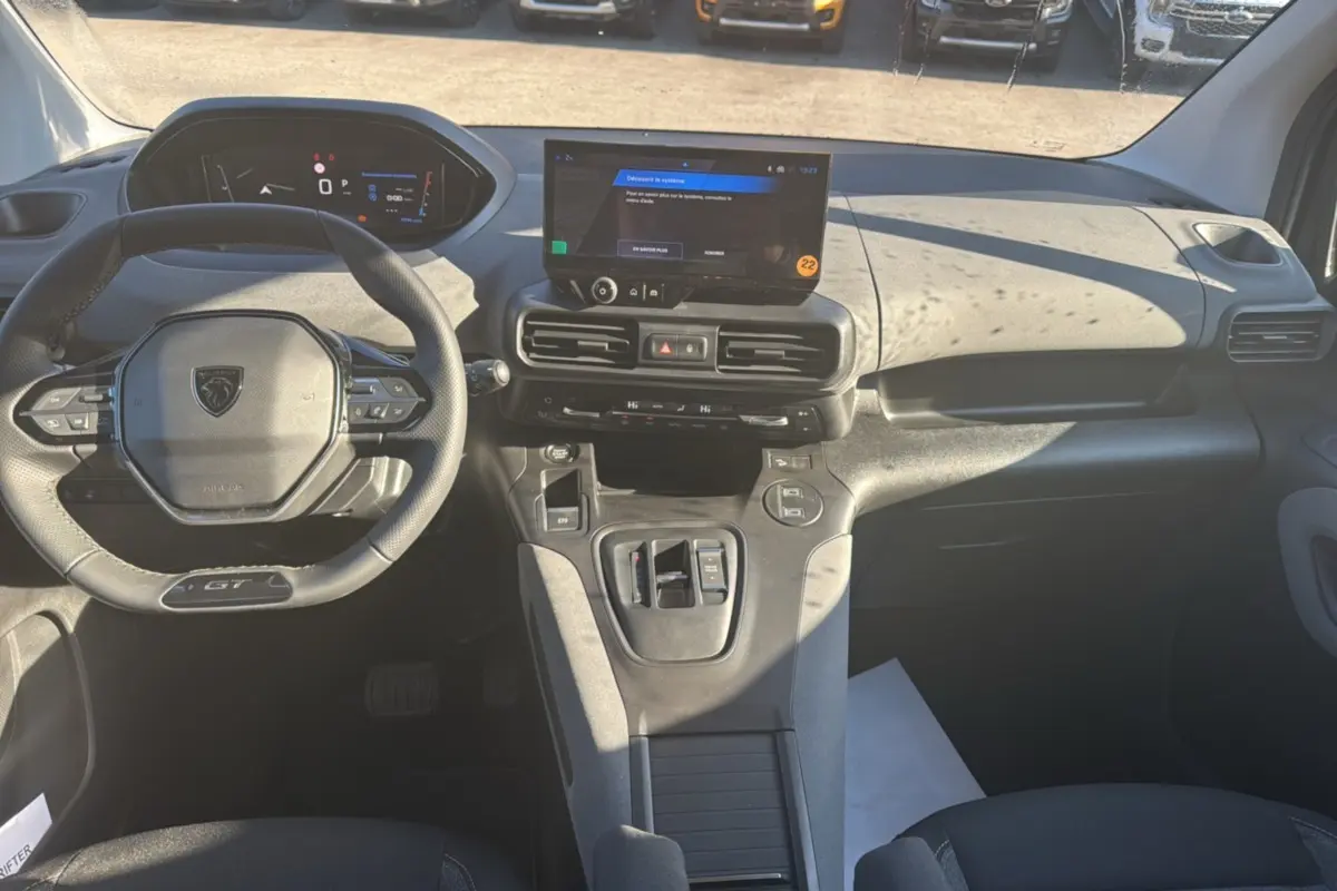 Vue intérieure avant du Peugeot Rifter GT Plus 2025, tableau de bord moderne avec écran tactile central et volant cuir multifonctions.