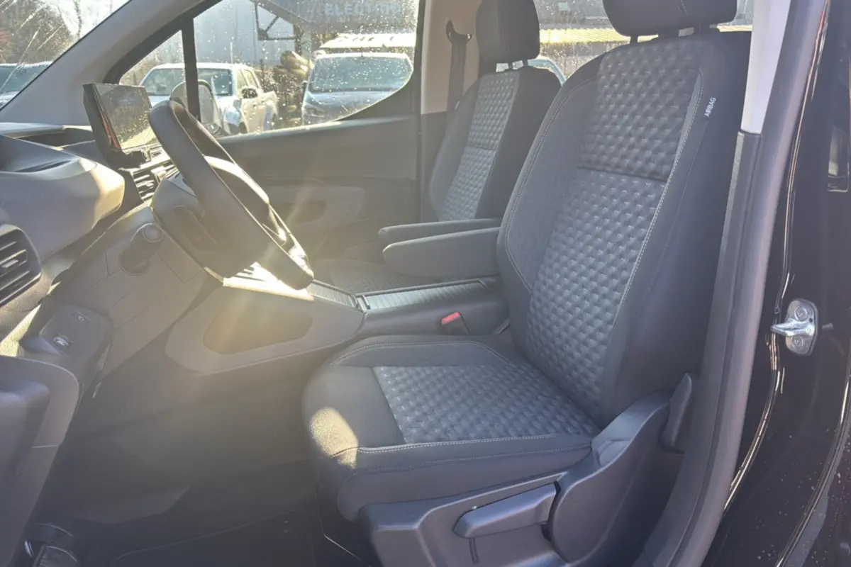 Vue intérieure côté conducteur du Peugeot Rifter noir perla nera 2025, sièges tissu gris avec accoudoir central.