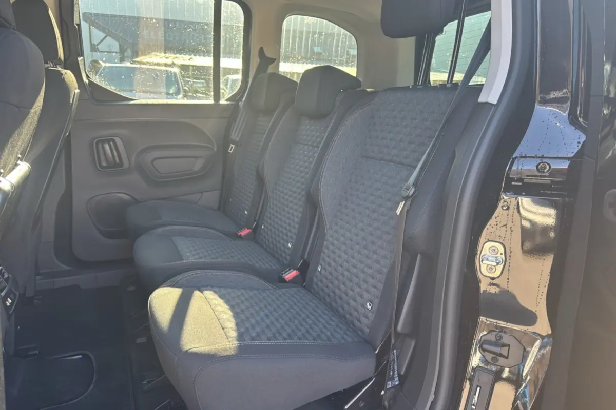 Vue latérale des sièges arrière en tissu gris foncé du Peugeot Rifter Noir Perla Nera avec porte coulissante ouverte.