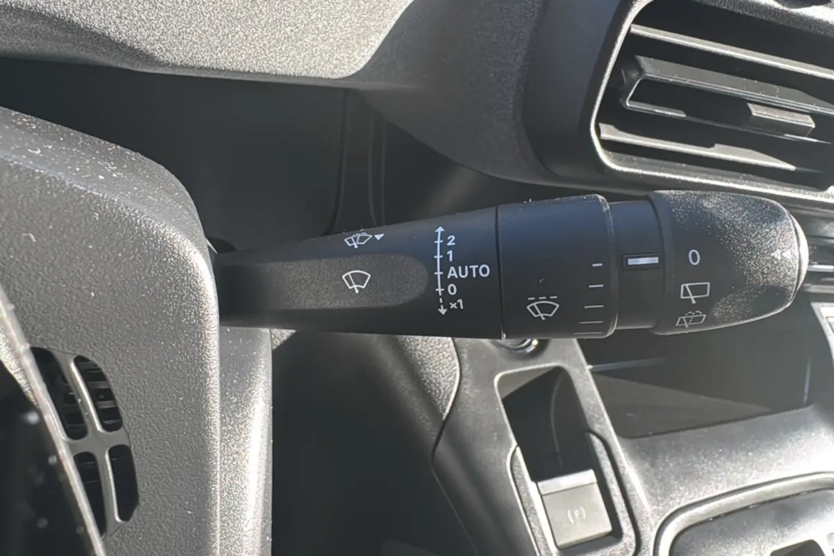 Gros plan sur la commande des essuie-glaces à gauche du volant dans l’habitacle du Peugeot Rifter noir Perla Nera 2025.