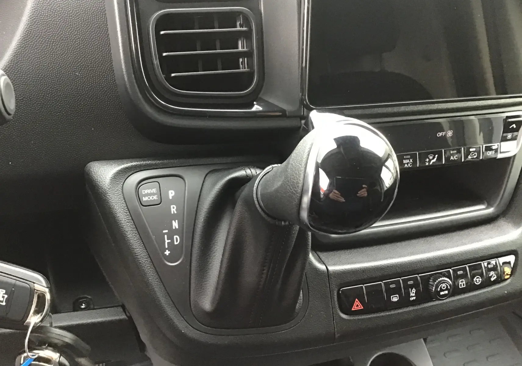 Gros plan sur le levier de vitesses automatique noir du Peugeot Boxer Fourgon blanc, avec commandes de climatisation et tableau de bord.