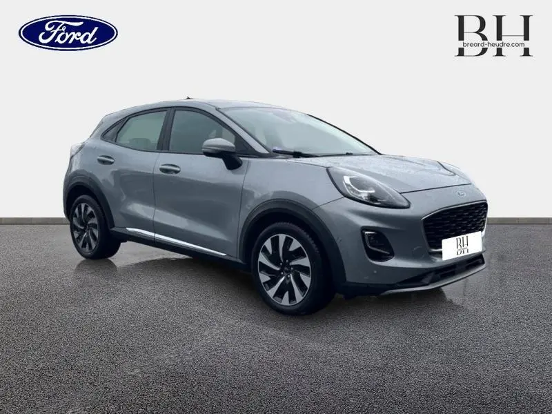 Ford Puma 2023 gris Solar métallisé en vue 3/4 avant droit, avec jantes alliage et calandre noire distinctive.