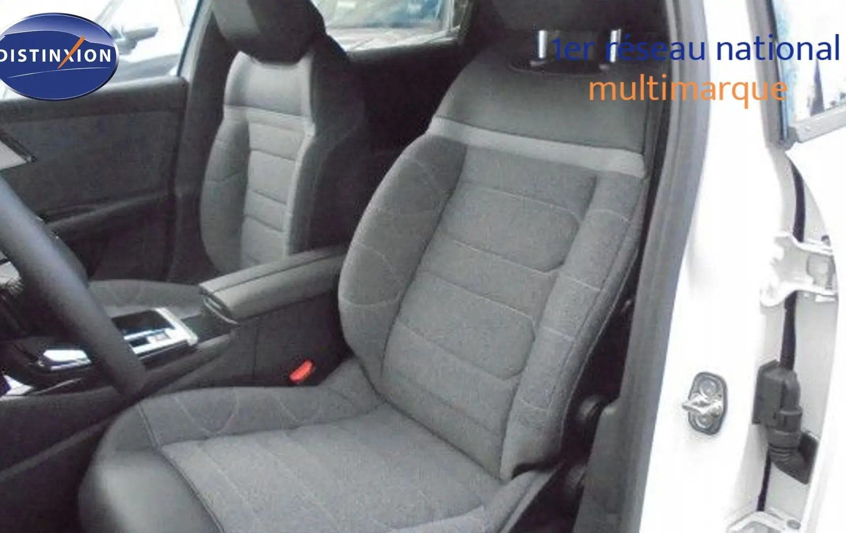 Intérieur du siège conducteur gris foncé d'une Citroën C5 X blanc métal, avec accoudoir et partie du tableau de bord visibles.