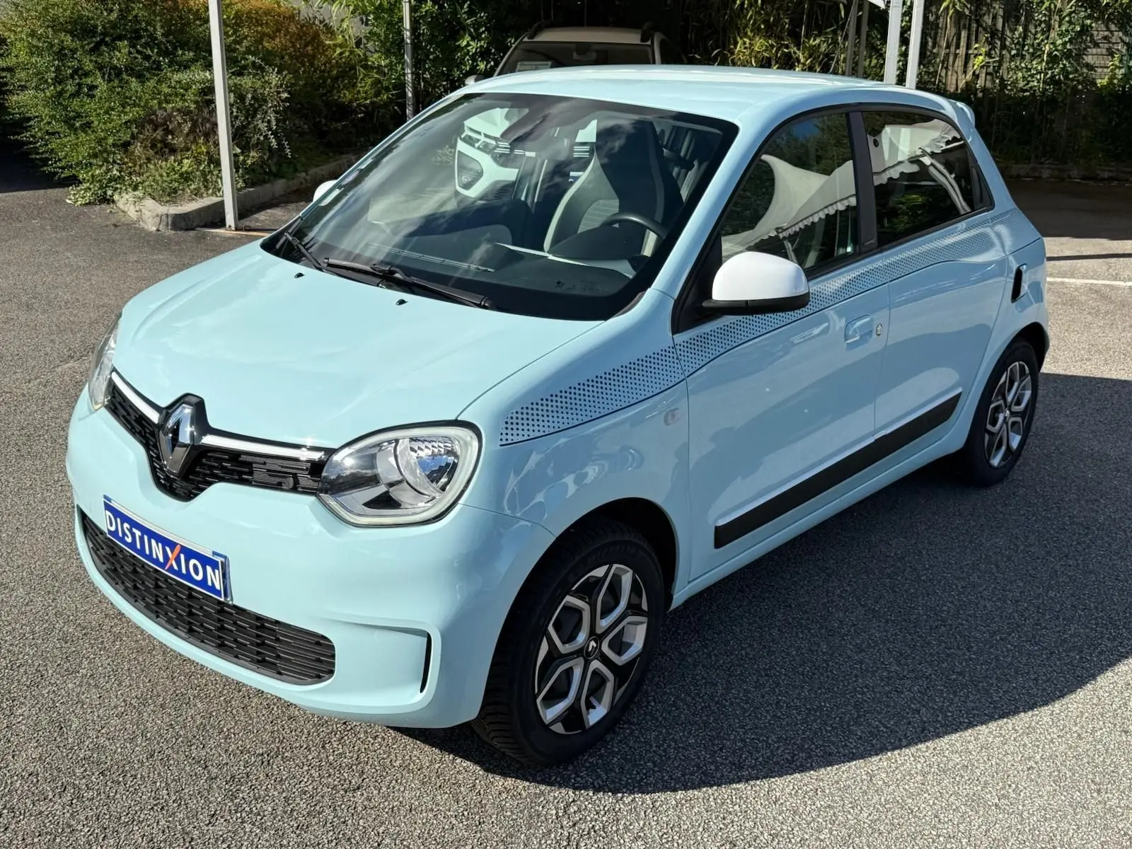 Renault Twingo III bleu dragée vue 3/4 avant droit avec jantes stylisées et bande décorative noire sur l'aile.