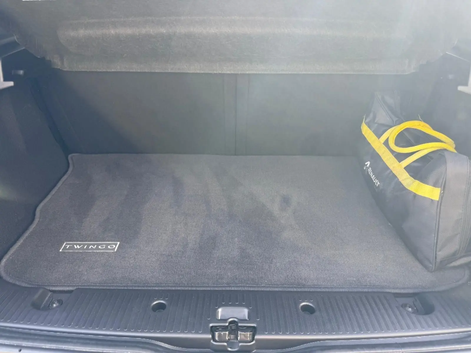 Coffre ouvert d'une Renault Twingo III bleu dragée, tapis de sol avec logo Twingo et sac d'accessoires Renault.