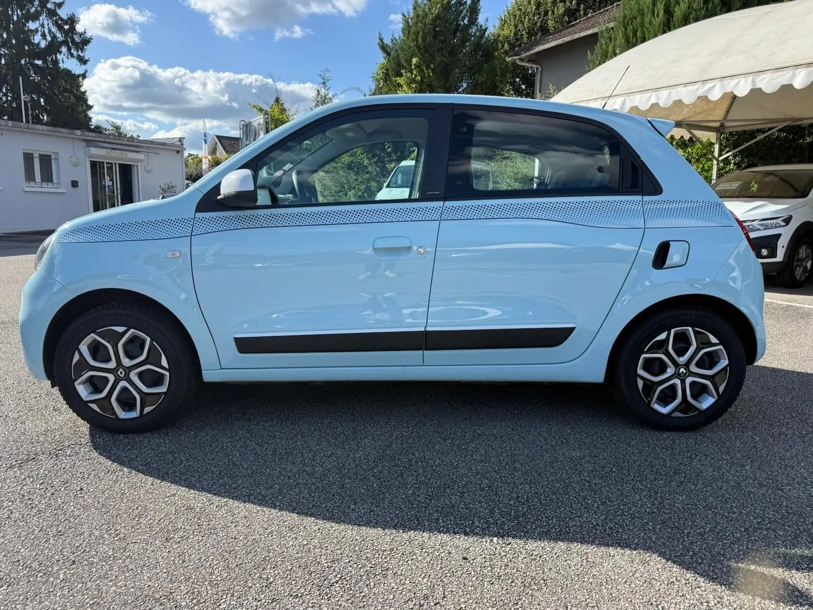 Profil droit d'une Renault Twingo III bleu dragée 2021 avec jantes à motifs hexagonaux et bande décorative noire sur la carrosserie.