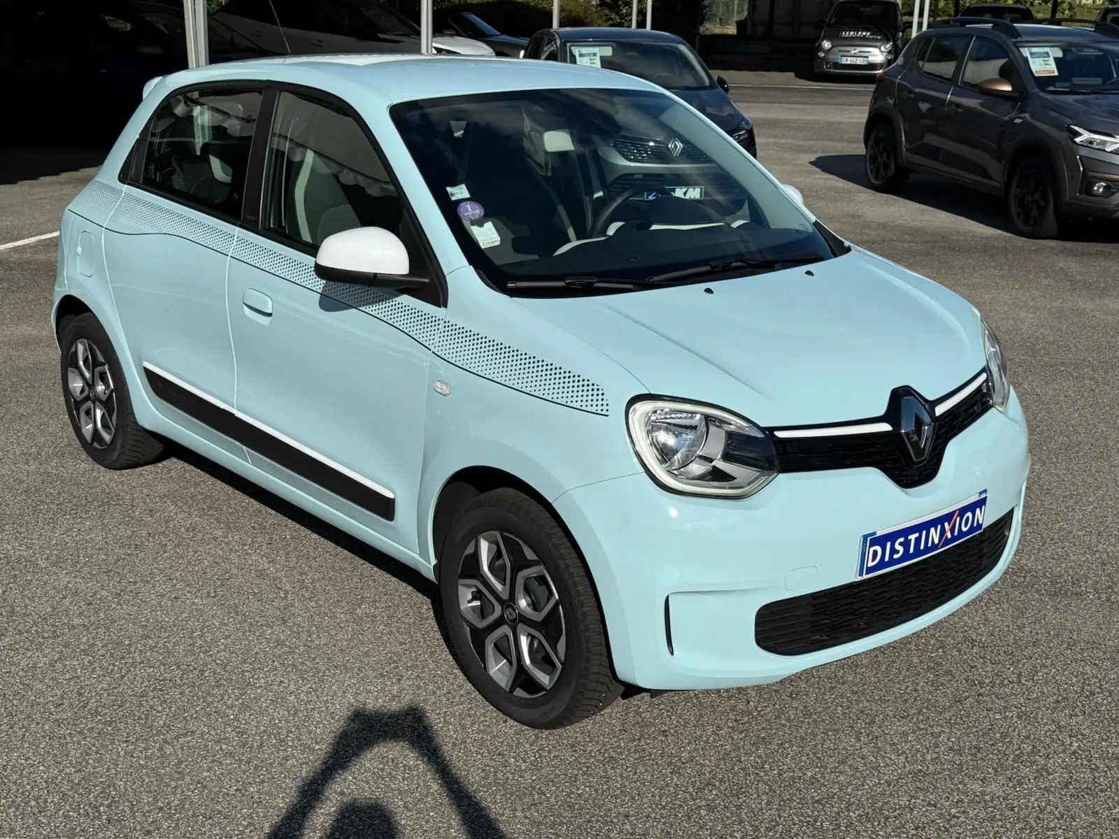 Renault Twingo III bleu dragée vue 3/4 avant droit, avec jantes spécifiques et décor pointillé sur l'aile avant.