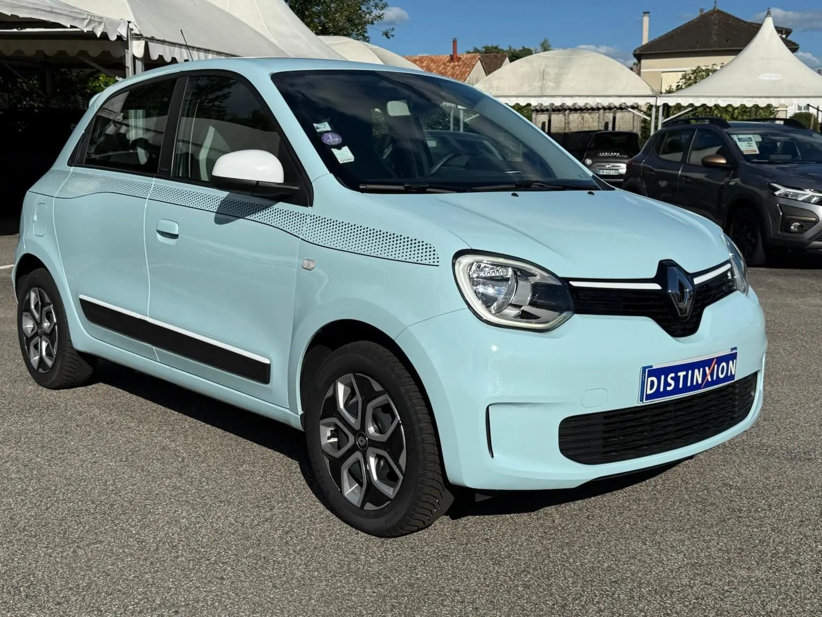 Renault Twingo III bleu dragée vue 3/4 avant droit avec détails noirs et jantes originales sur parking extérieur.