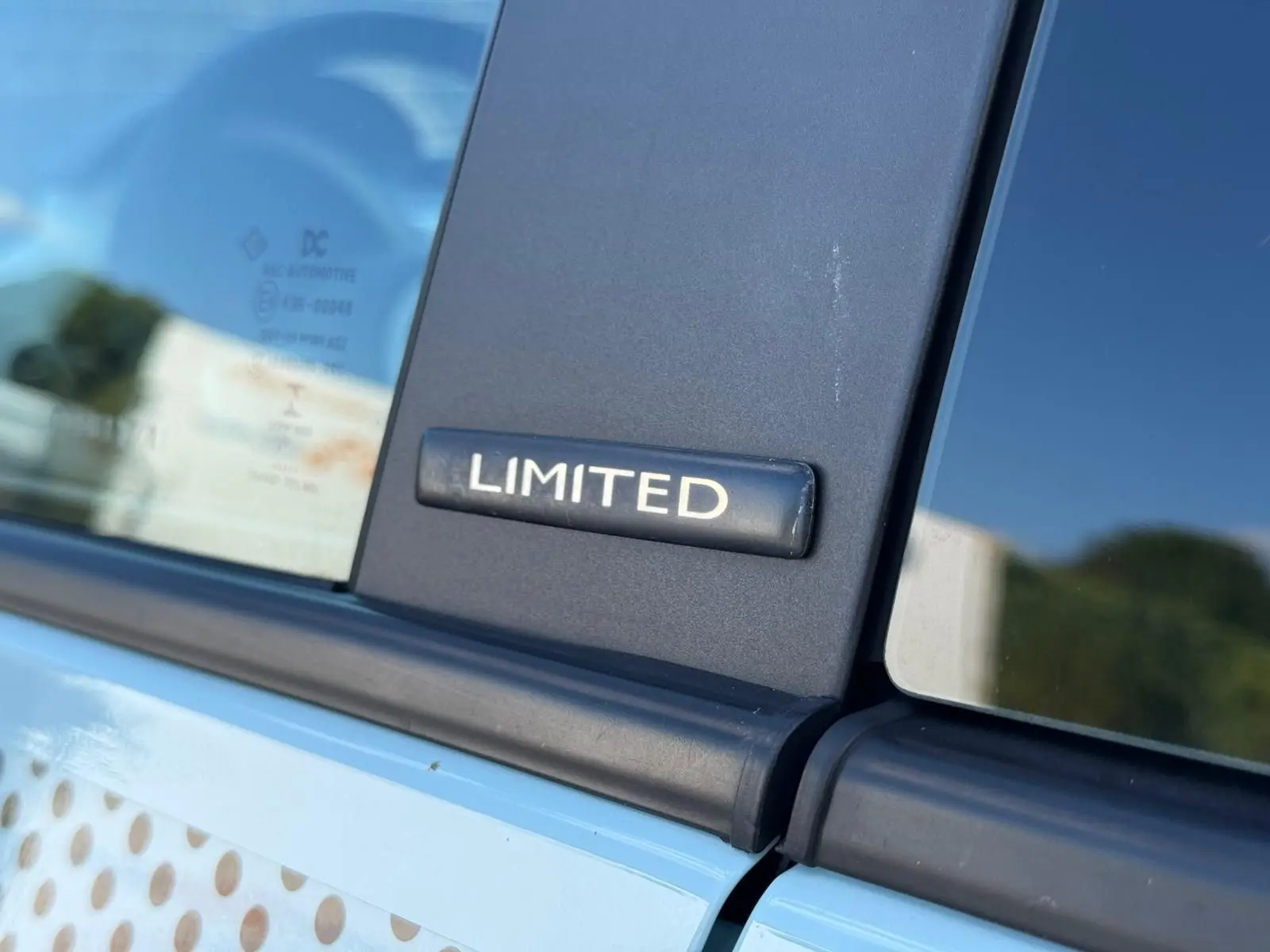 Gros plan sur l'écusson "LIMITED" noir sur la porte d'une Renault Twingo III bleu dragée, côté gauche.